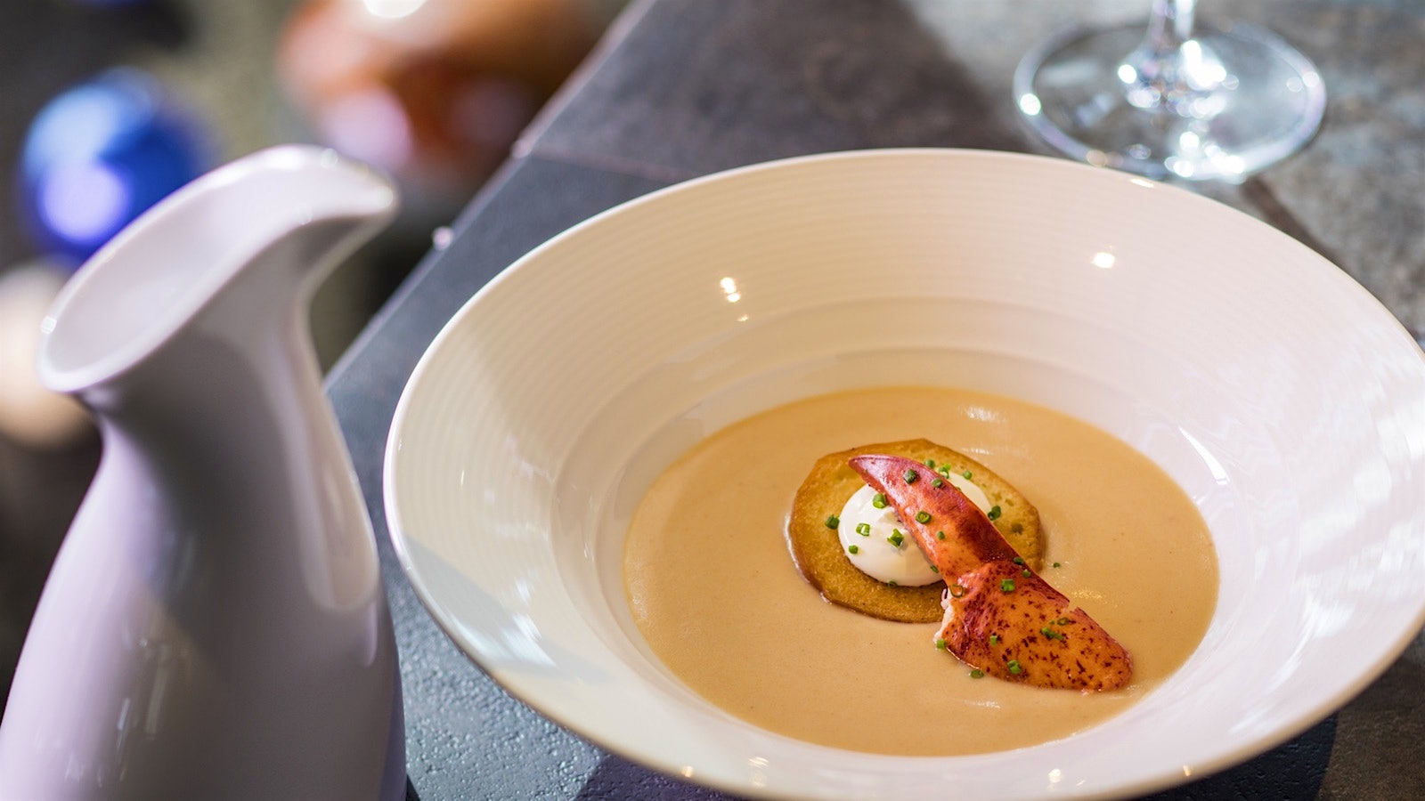 Bowl of Maine lobster bisque topped with lobster claw meat and accompanied by a pitcher and a glass of wine